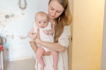 Beautiful young mother blonde in light clothes holds in her arms a newborn daughter 2 months