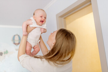Beautiful young mother blonde in light clothes holds in her arms a newborn daughter 2 months