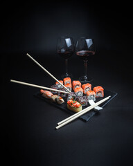Sushi with red wine on a dark restaurant background. Chopsticks. A glass of wine. Soy sauce. Rolls and sushi. Japanese cuisine.