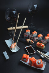 Sushi with red wine on a dark restaurant background. Chopsticks. A glass of wine. Soy sauce. Rolls and sushi. Japanese cuisine.