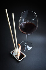 Sushi with red wine on a dark restaurant background. Chopsticks. A glass of wine. Soy sauce. Rolls and sushi. Japanese cuisine.