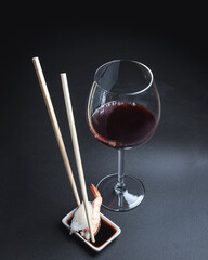 Sushi with red wine on a dark restaurant background. Chopsticks. A glass of wine. Soy sauce. Rolls and sushi. Japanese cuisine.