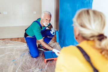 Happy senior couple renovating their home. They are painting a wall together.