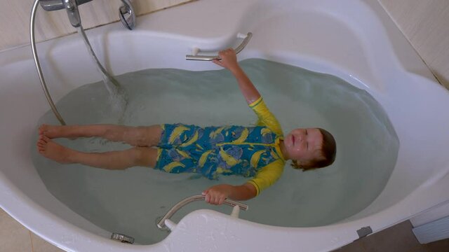 Funny kid in bright bathing suit swims and bathes in bathroom