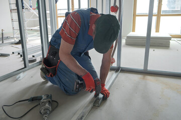 worker screws the screw into the drywall rack