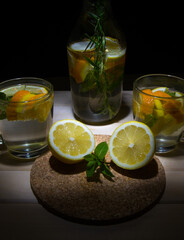 A bottle and two glasses with a drink, with mint lemon, orange is on the table