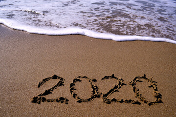 The year 2020 is drawn on sand with foam waves