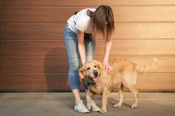 Woman in blue jeans stroking dog outdoors in afternoon.