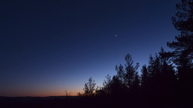 Time lapse sky darkens at nightfall over trees on clear sky evening