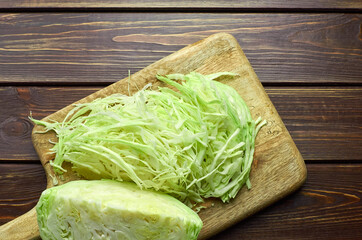 Cutting board with shredded white cabbage salad on dark wooden background.