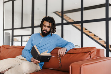 Handsome young african man sitting on a leather couch at home