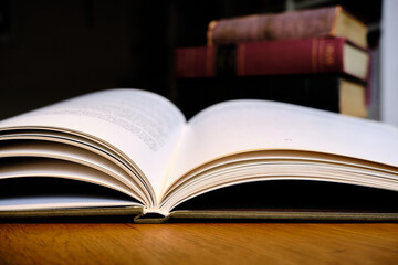 Close up of open text book on wooden desk in library. Old books and bookshelf background. Education concept. Selective focus