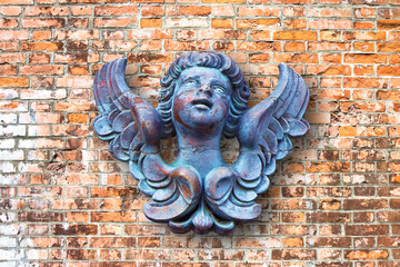 Wooden sculpture of an italian angel against a brick wall