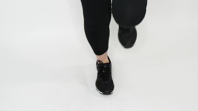 A Senior Woman Bouncing Rhythmically On One Foot In Black Leggings And Shoes With A White Background.