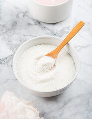 Collagen protein powder in bowl with wooden spoon on marble table. Vertical shot