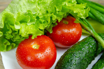 beautiful fresh, juicy vegetables with drops of water on a white plate: fresh peppers, tomatoes, cucumbers, lettuce, dill, green onions