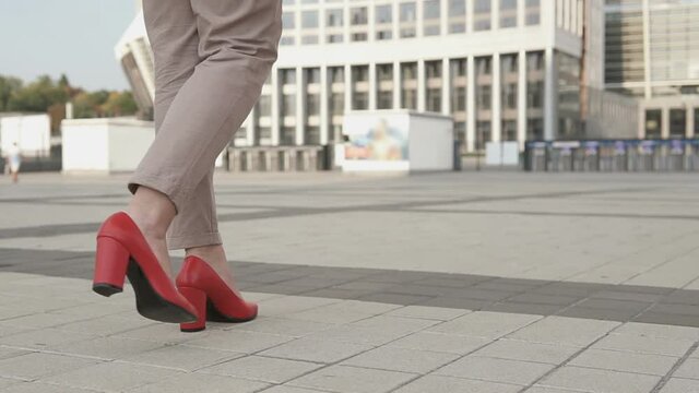 Business female legs in red shoes with high heels. Successful business girl goes towards the business center.