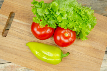 Fresh juicy vegetables peppers, tomatoes, cucumbers lettuce leaves with water drops are beautifully laid out on a wooden Board close-up. Vegetables are in the form of a funny face, top view