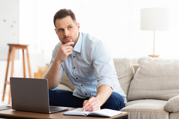 Man using laptop at home and writing notes in notepad