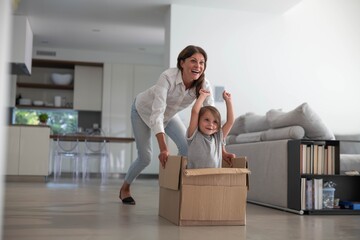 Authentic shot of carefree happy smiling mother and daughter are having fun to racing with empty box just moved into a new house.