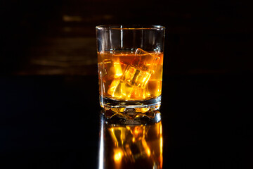Glass of whiskey with ice cubes on black table