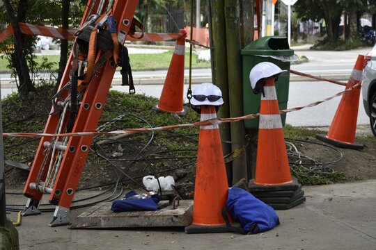 White hard hat on top of a safety cone with extension ladder on a sidewalk