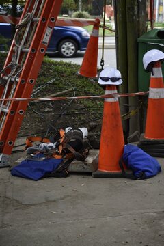 Vertical shot of a white hard hat on top of a safety cone with an extension ladder on a sidewalk