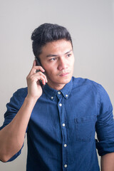 Young handsome Asian businessman thinking while talking on the phone