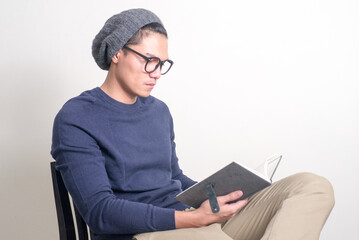 Portrait of young handsome Asian hipster man sitting while reading book