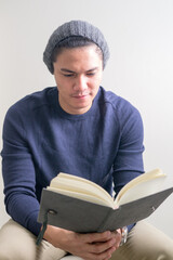 Portrait of young handsome Asian hipster man sitting while reading book