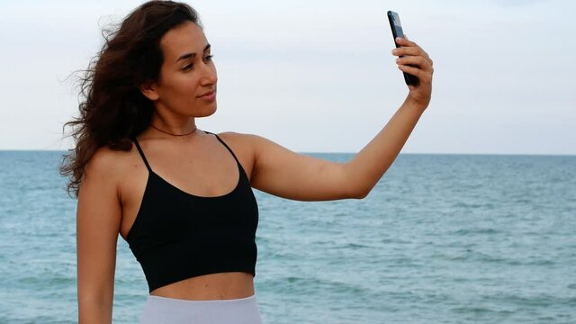 Beautiful sexy tanned woman makes selfie on the background of the sea. Woman makes summer photo at sunset on the sea.
