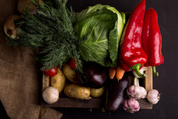 Assortment of fresh raw vegetables in a wooden box against black background. Organic local food.
