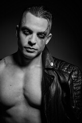 Fototapeta na wymiar A man with embossed muscles and a naked torso in a leather jacket
