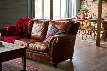 Cozy brown leather sofa with a plaid in a warm interior