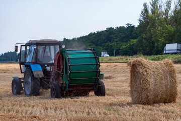 Obraz premium A tractor with a trailed bale making machine collects straw rolls in the field and makes round large bales