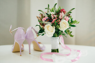 bridal bouquet of white and pink roses, boxwood branches, aronia, veronica flowers, pink and white ribbons on the table and pink shoes of the bride
