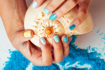 woman hands holding sea shell and sea salt with manicured nails