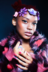 young pretty african american woman in spotted fur coat and flowers jewelry posing on black background