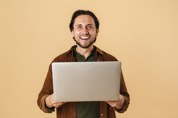 Image of pleased unshaven man smiling while using laptop
