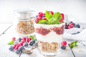 Yogurt parfafait with granola and berries. Sweet and healhty breakfast dessert in glass with granola, Yogurt, blueberries and raspberries. White wooden background top view