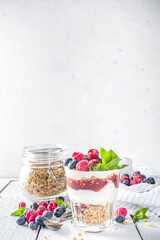 Yogurt parfafait with granola and berries. Sweet and healhty breakfast dessert in glass with granola, Yogurt, blueberries and raspberries. White wooden background top view