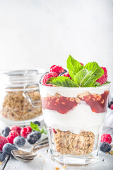 Yogurt parfafait with granola and berries. Sweet and healhty breakfast dessert in glass with granola, Yogurt, blueberries and raspberries. White wooden background top view