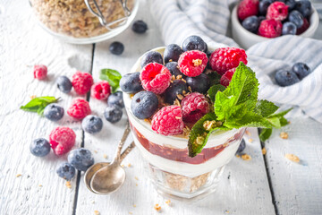 Yogurt parfafait with granola and berries. Sweet and healhty breakfast dessert in glass with granola, Yogurt, blueberries and raspberries. White wooden background top view