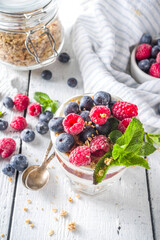 Yogurt parfafait with granola and berries. Sweet and healhty breakfast dessert in glass with granola, Yogurt, blueberries and raspberries. White wooden background top view