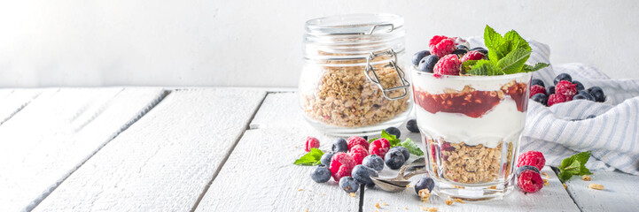 Yogurt parfafait with granola and berries. Sweet and healhty breakfast dessert in glass with granola, Yogurt, blueberries and raspberries. White wooden background top view