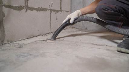 A worker vacuums a concrete floor with a vacuum cleaner. vacuum cleaner construction on the...