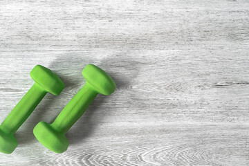 Green dumbbells on a wooden background for fitness classes. Space for text.
