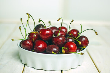Ripe tasty juicy cherry in a white plate next to field daisies on a white background. Berry still life with flowers, summer background
