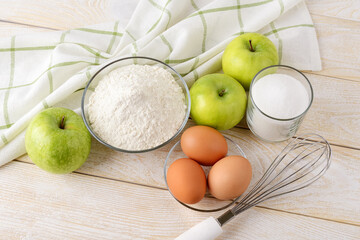 Apple pie raw ingredients: sour green apples, wheat flour, sugar and eggs on a white wood table. Easy recipe for sweet homemade baking. Cook at home.