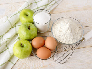 Raw ingredients prepared for baking apple pie: sour green apples, wheat flour, sugar and eggs on a white wood table. Easy recipe for sweet homemade baking. Cook at home.